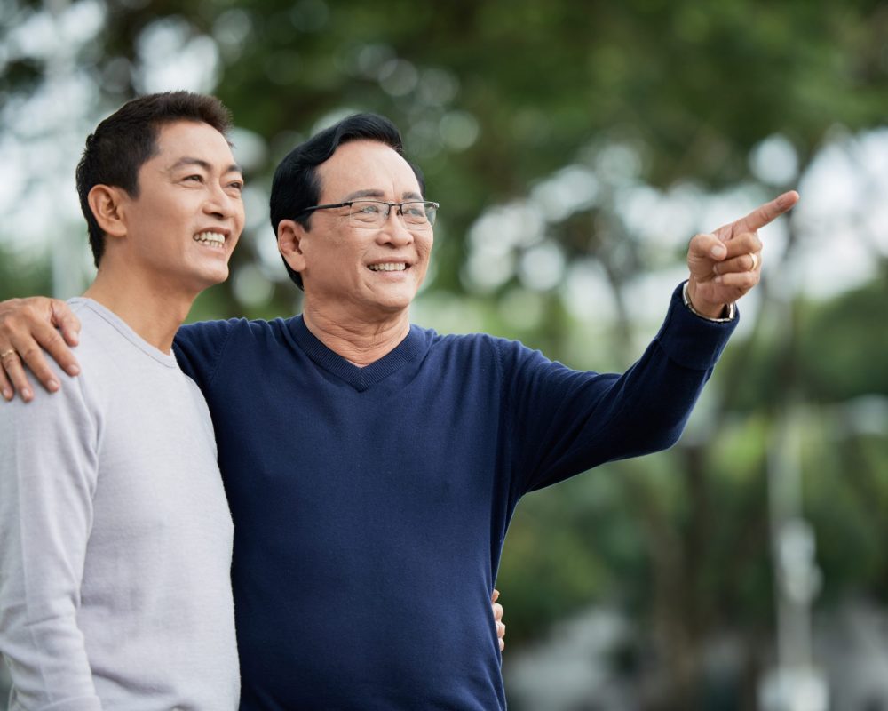Elderly,Asian,Man,Smiling,And,Pointing,At,Distance,While,Embracing